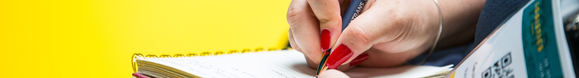 a woman takes notes in a notebook and listens to a speaker 