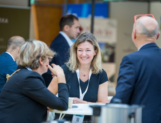 Group of smiling people chatting during a coffee break at the supply chain top logistics europe event in front of the booths